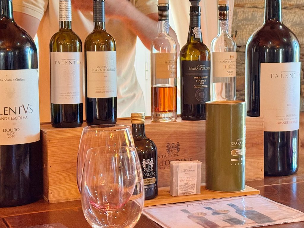 A selection of wine and liquor bottles displayed on a wooden counter with two empty wine glasses and tasting notes in front.