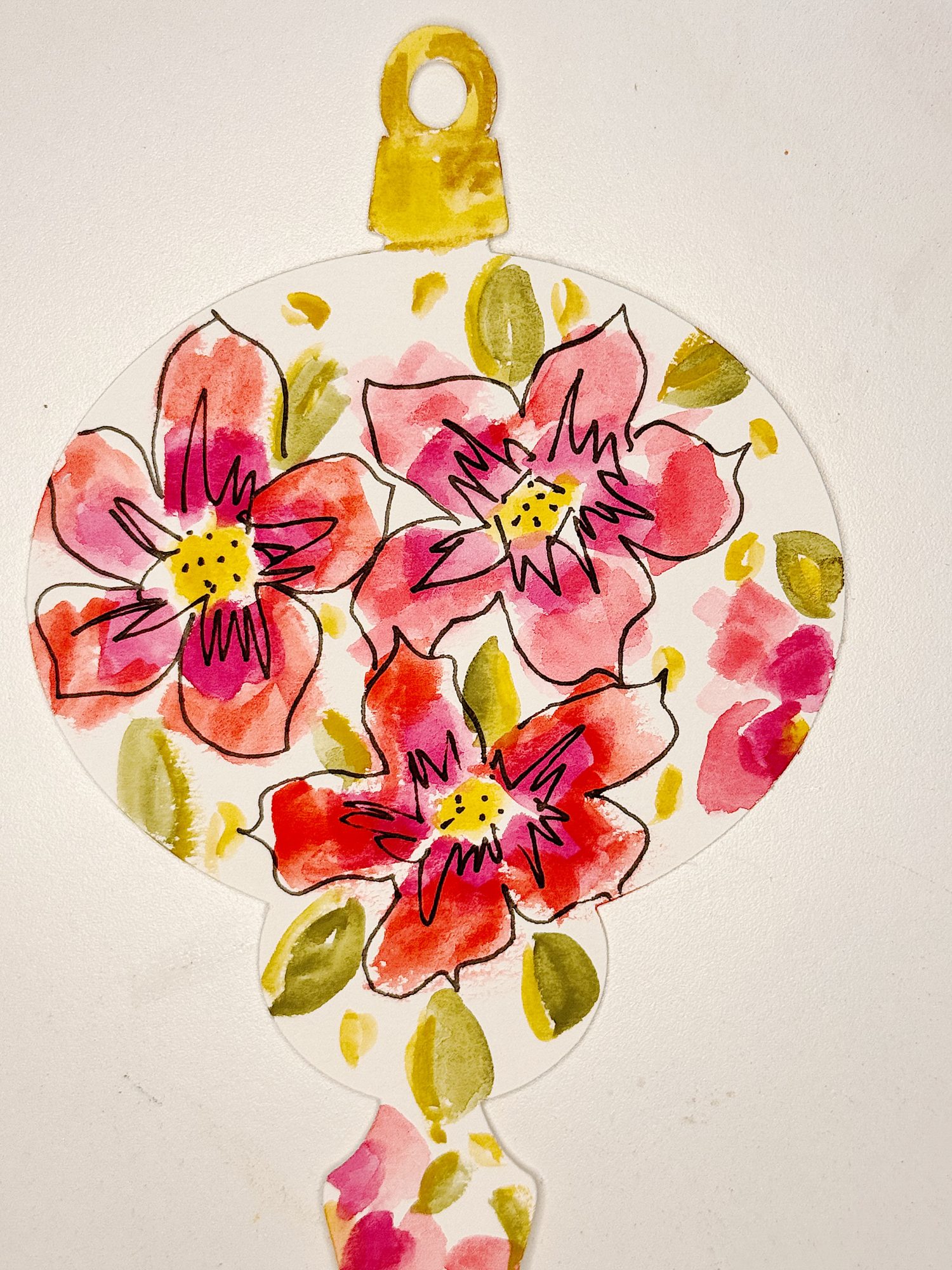 A hand-painted ornament-shaped paper features three red and pink flowers with green leaves on a white background.