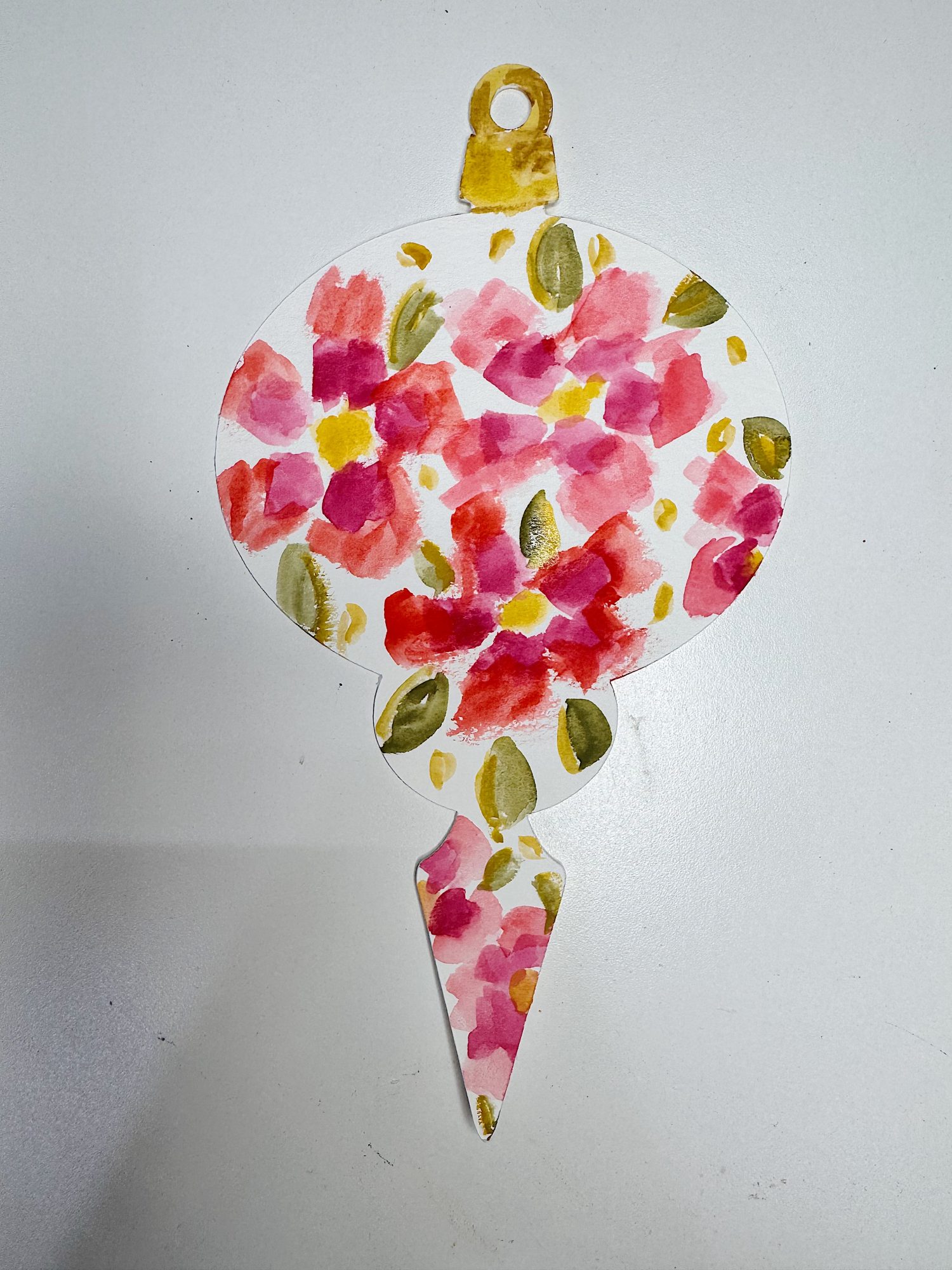 A paper ornament shaped like a bulb with a pointed tip, decorated with red and pink watercolor flowers and green leaves on a white background.