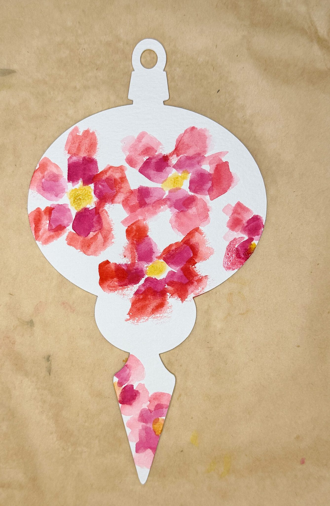 A paper ornament cutout painted with red and pink watercolor flowers, placed on a brown surface.