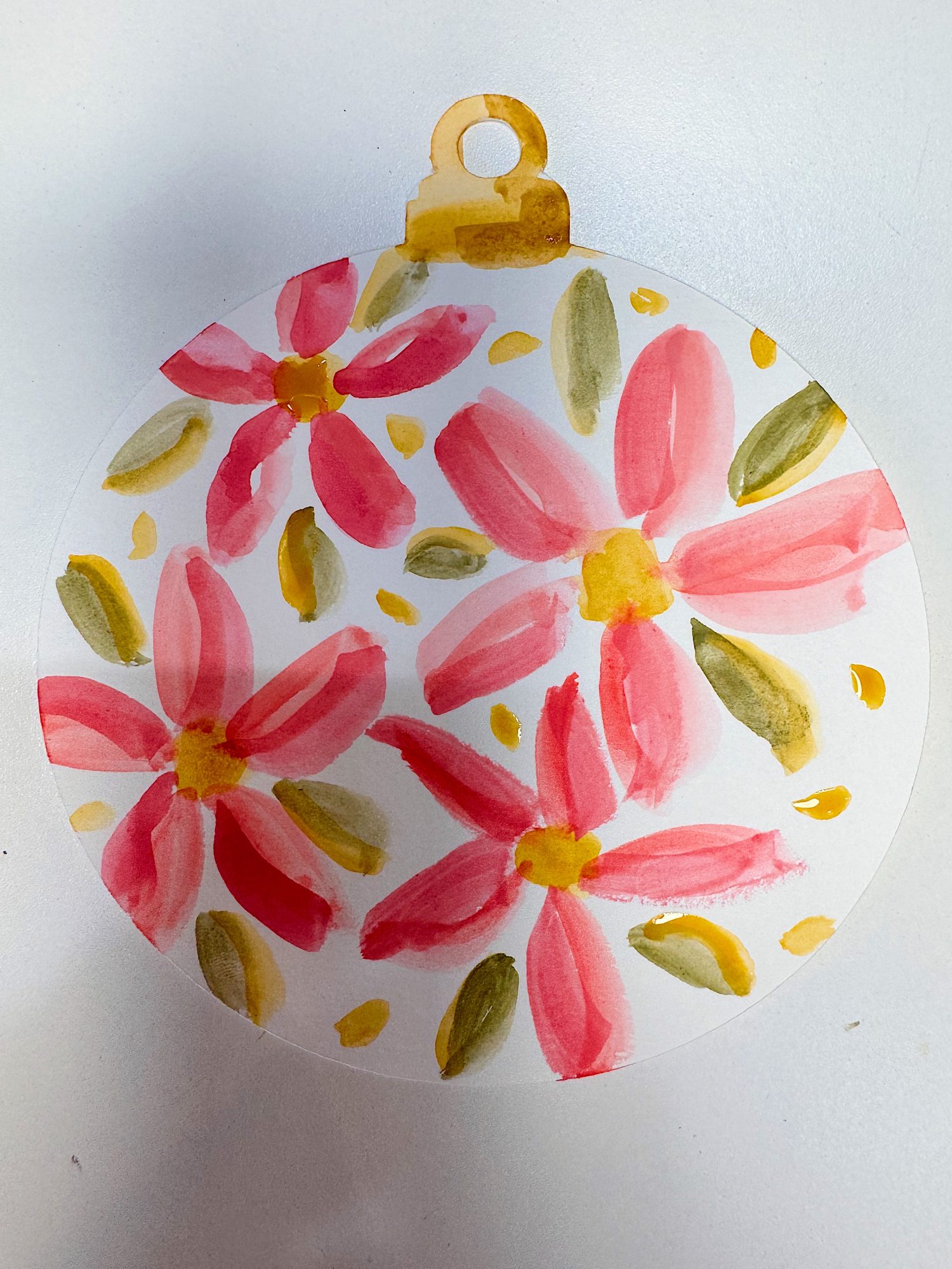 A round ornament-shaped paper features hand-painted pink flowers with yellow centers and green leaves on a white background.