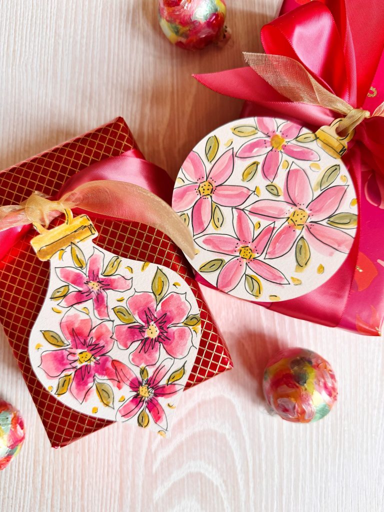 Two rectangular gifts wrapped in red paper and pink ribbon, decorated with hand-painted floral ornaments and surrounded by colorful round candies.
