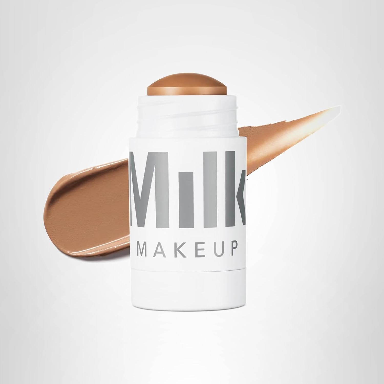 A Milk Makeup stick with a swipe of brown cream makeup behind it on a plain white background—perfect for scoring during Amazon Prime Big Deal Days.