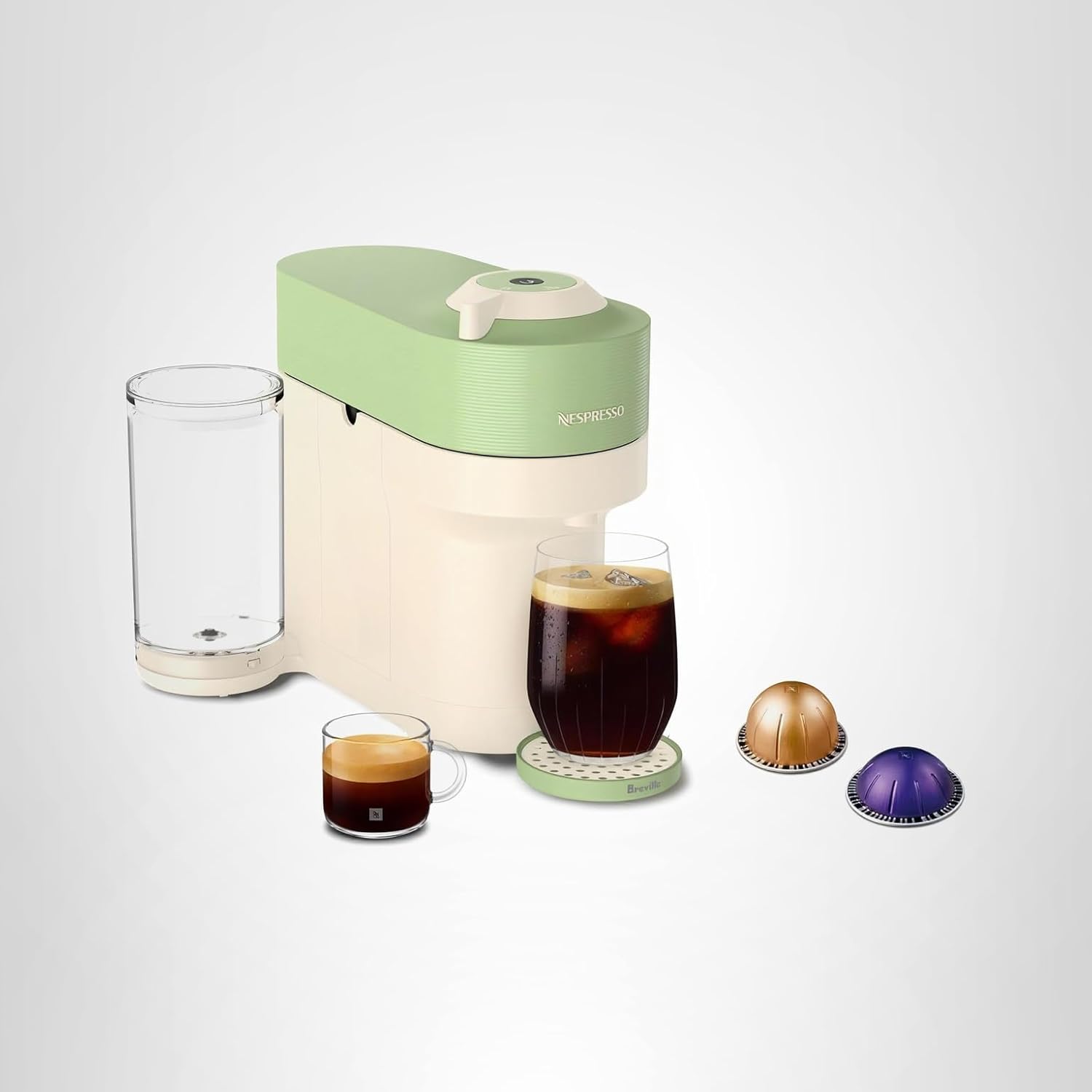A cream and light green Nespresso coffee machine with a clear water tank, two glass cups of coffee, and three coffee capsules on a white background—perfect for brewing during Amazon Prime Big Deal Days.