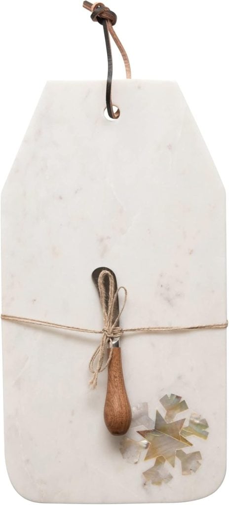 A rectangular white marble cheese board with a leather strap, featuring a small wooden-handled spreader tied with twine and a decorative inlay in one corner.