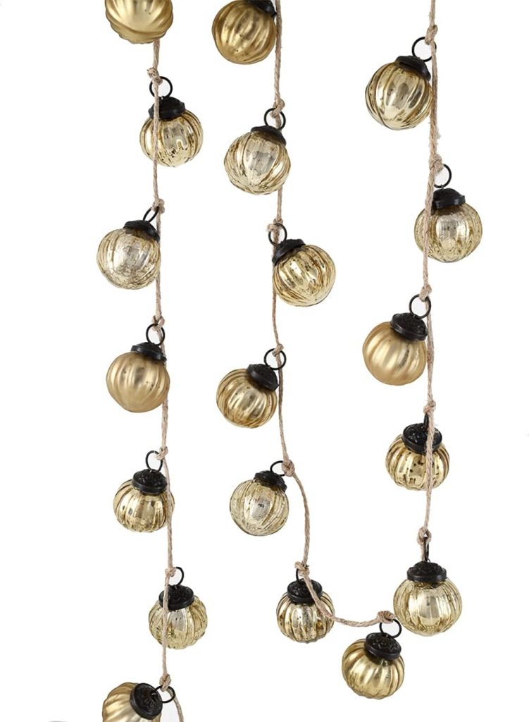 Strings of small, round, gold and clear glass ornaments are hanging vertically against a white background.