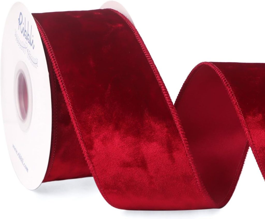 A spool of red velvet ribbon with a wavy section extended outward against a white background.