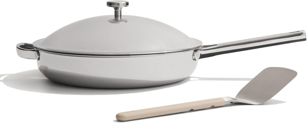 A stainless steel frying pan with a lid and a matching spatula placed in front of it on a white background—perfect for preparing Marry Me Chicken and other delicious dishes.