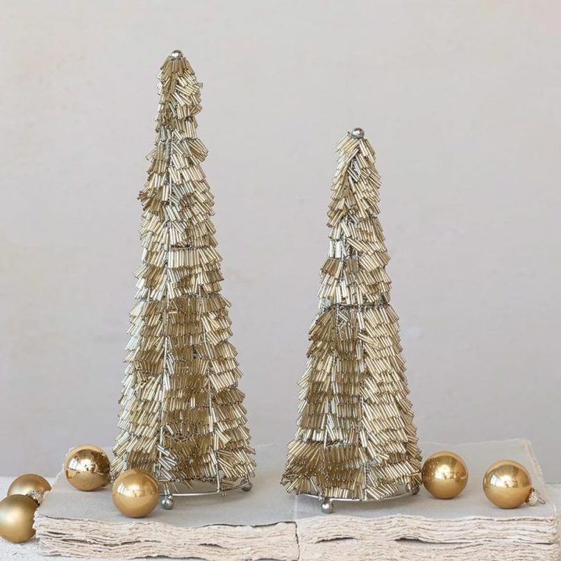 Two gold decorative Christmas trees and several gold ornaments, showcasing classic Christmas colors, are arranged on a textured white surface against a plain light background.