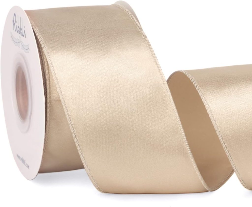 A spool of wide, light beige satin ribbon with a slightly shiny finish, partially unrolled and curling in the foreground.