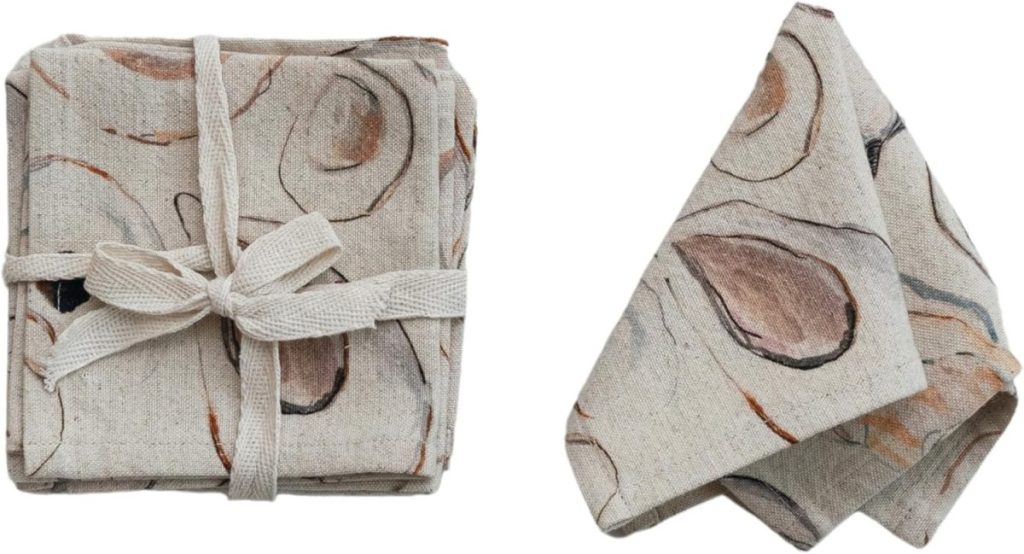 Two linen napkins with an oyster shell print; one is folded and tied with a fabric ribbon, the other is unfolded and draped—perfect for refreshing your table setting during Amazon Prime Big Deal Days.