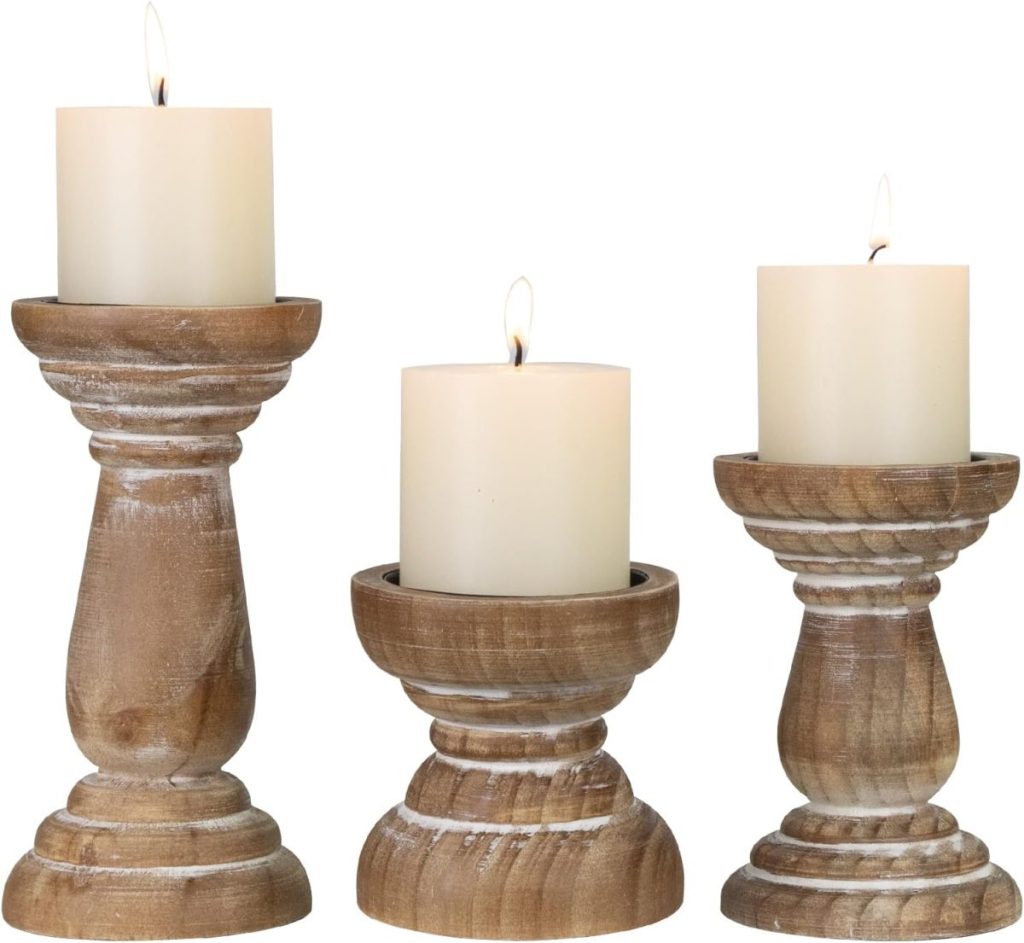 Three lit pillar candles on rustic wooden candle holders of varying heights, arranged side by side with charming burlap Christmas trees, set against a plain background.