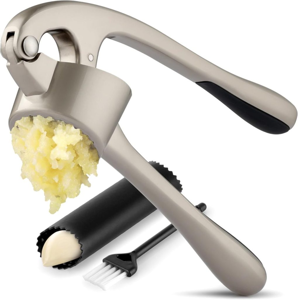 A metal garlic press with minced garlic inside, accompanied by a garlic peeler tube and a small cleaning brush on a white background—perfect for prepping Marry Me Chicken.