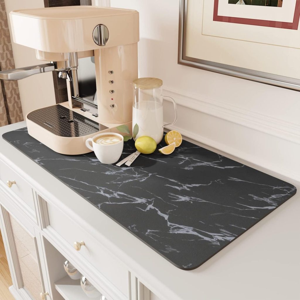 A coffee machine, a cup of latte with latte art, a glass pitcher, and sliced lemons are arranged on a black marble countertop mat—perfect for upgrading your kitchen ahead of Amazon Prime Big Deal Days.