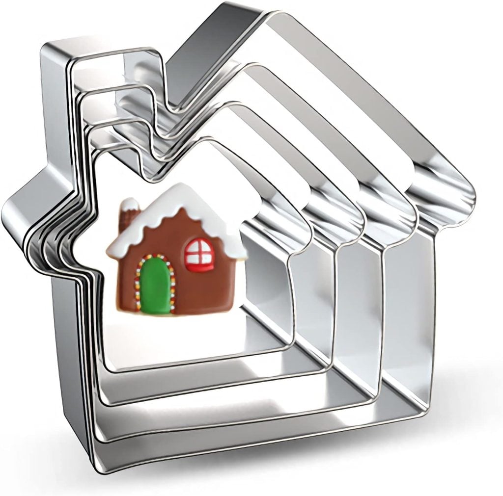Five nested metal house-shaped cookie cutters with a decorated gingerbread house cookie placed in the center.