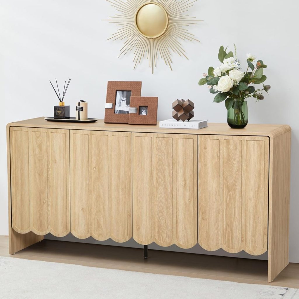 A light wood sideboard with scalloped doors displays framed photos, books, a vase with flowers, and decor items beneath a sunburst wall mirror—perfect for updating your space during Amazon Prime Big Deal Days.