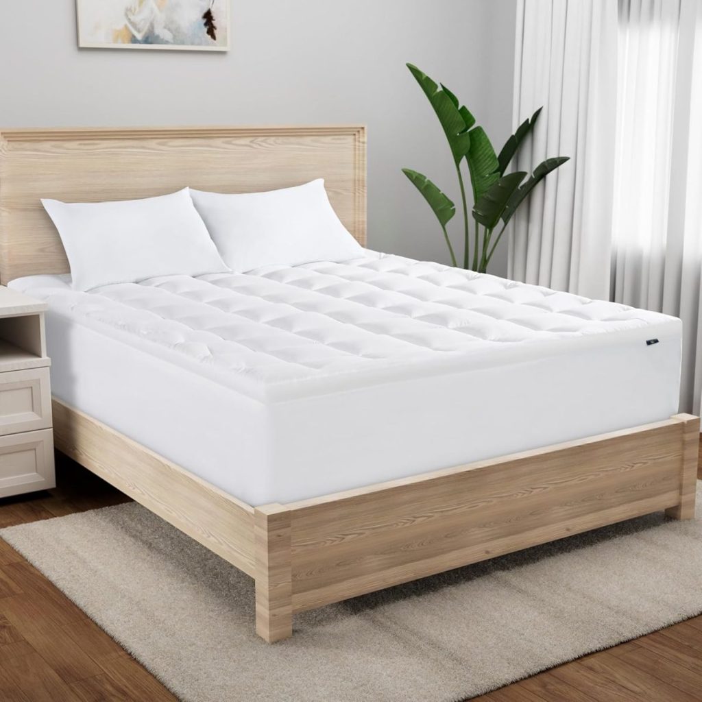 A neatly made bed with a white mattress topper, two white pillows, a wooden frame, and a bedside table is complemented by a potted plant in a bright, modern bedroom—perfect inspiration for Amazon Prime Big Deal Days finds.