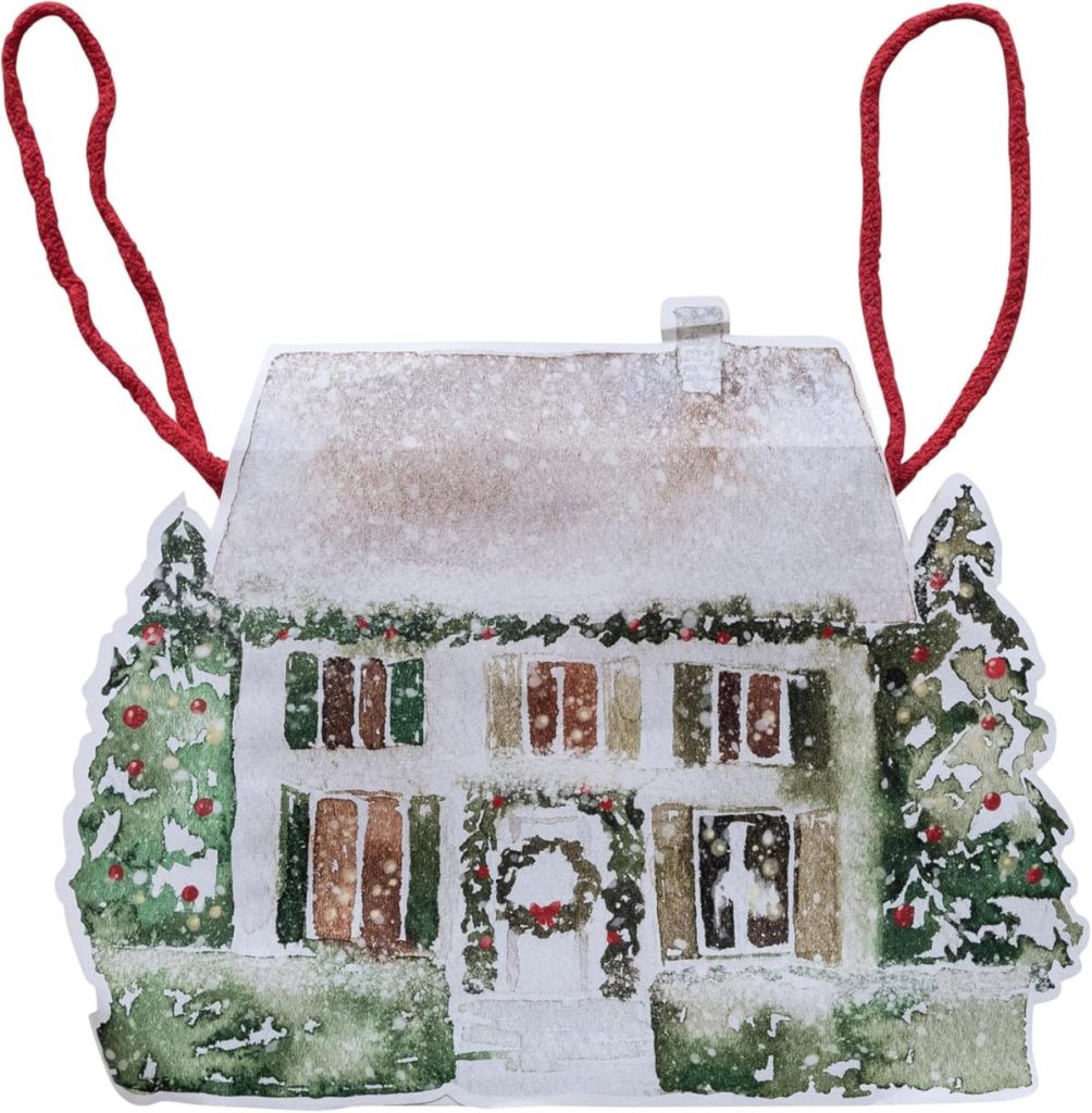 A painted ornament of a snow-covered house with two decorated trees, wreaths, and red string for hanging.