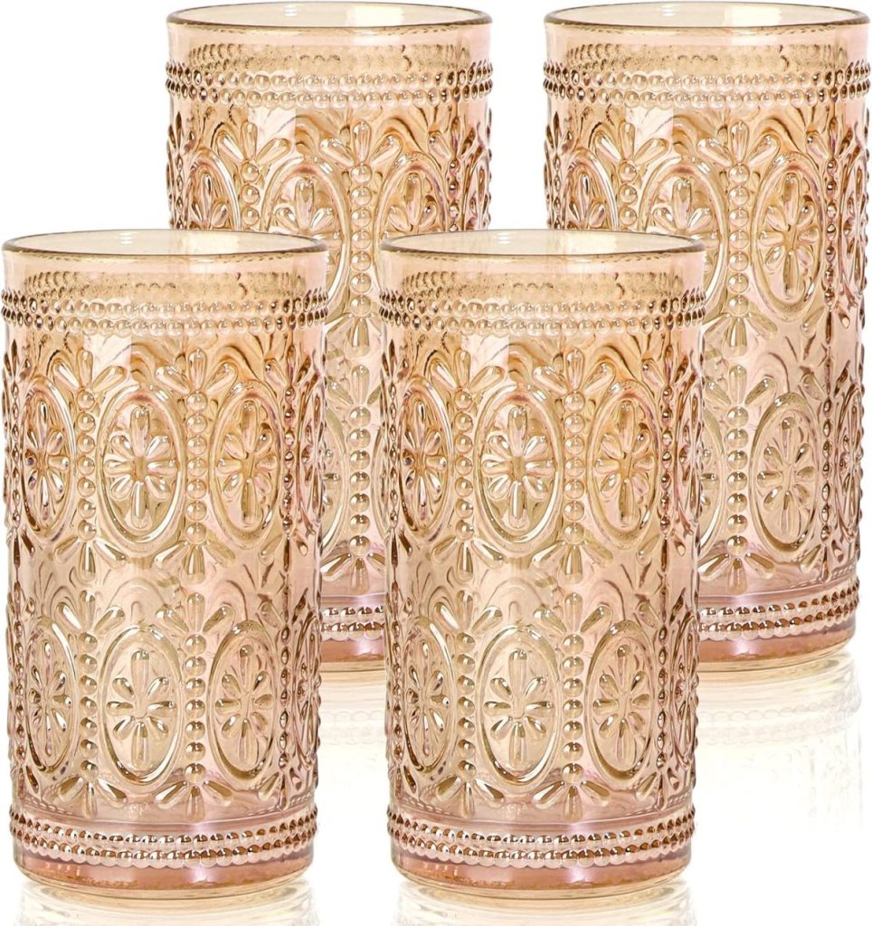 Four intricately patterned, amber-tinted drinking glasses are arranged together on a reflective surface.