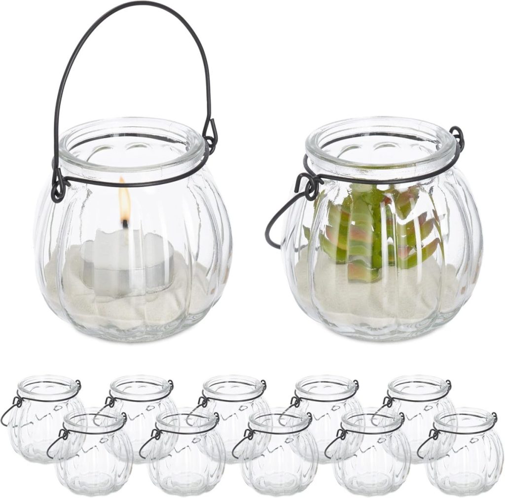 Twelve clear glass lantern holders with metal handles, two shown with contents: one holding a lit tealight candle and one with sand and a small decorative object inside.