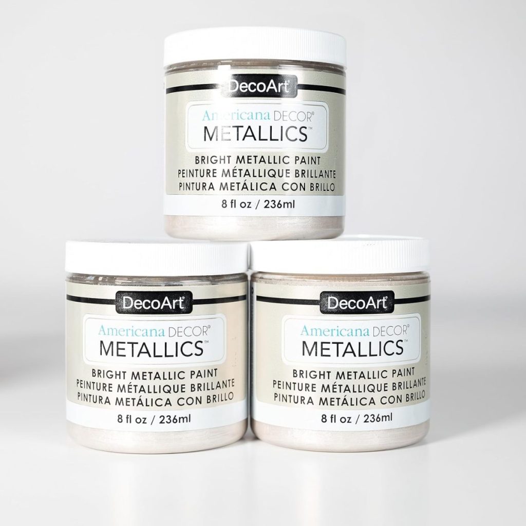 Three jars of DecoArt Americana Decor Metallics bright metallic paint, each containing 8 fl oz (236 ml), are arranged on a white surface with one jar on top of two others.