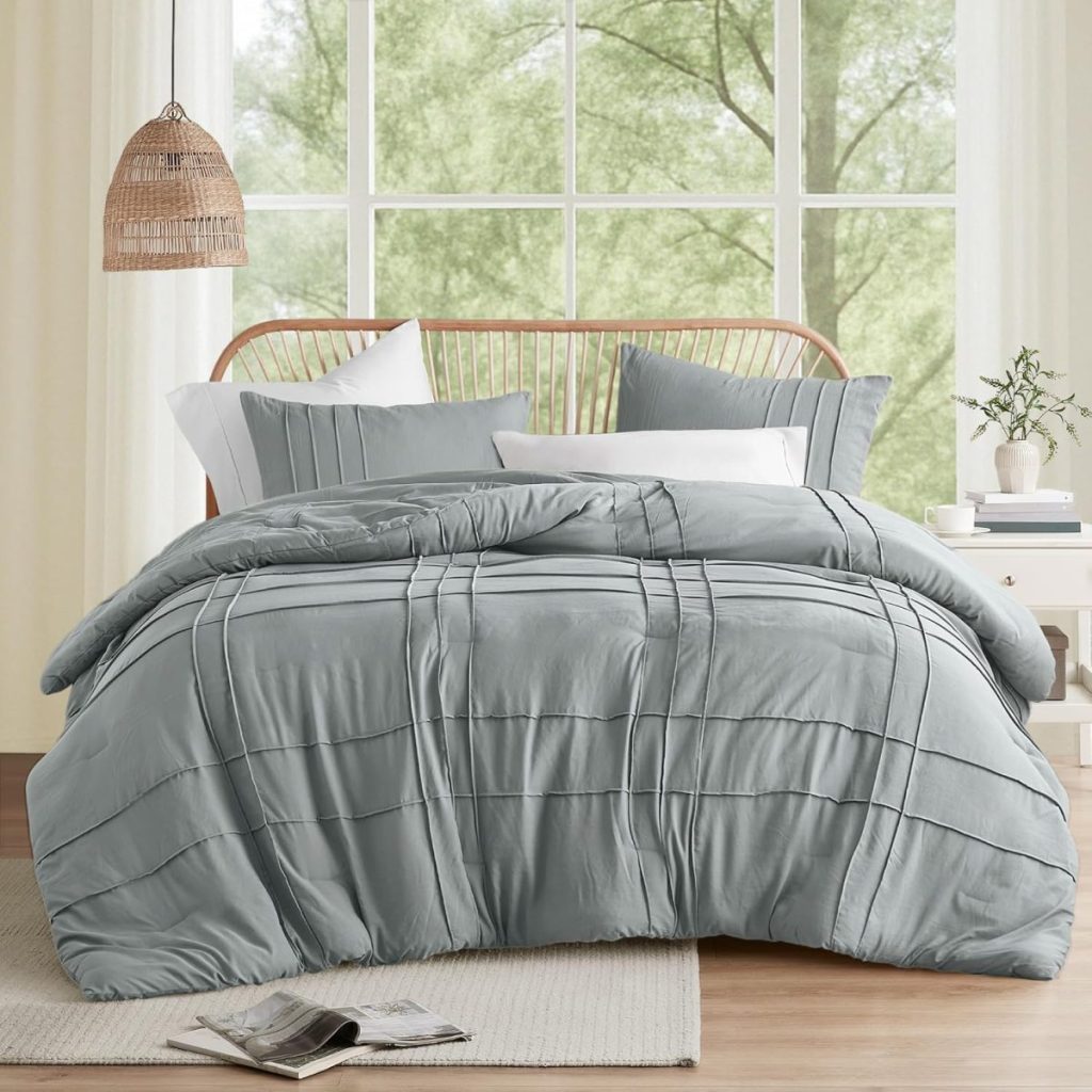 A neatly made bed with gray bedding and pillows sits in front of large windows; an open book and a magazine on the light floor inspire cozy relaxation—perfect for lounging during Amazon Prime Big Deal Days.