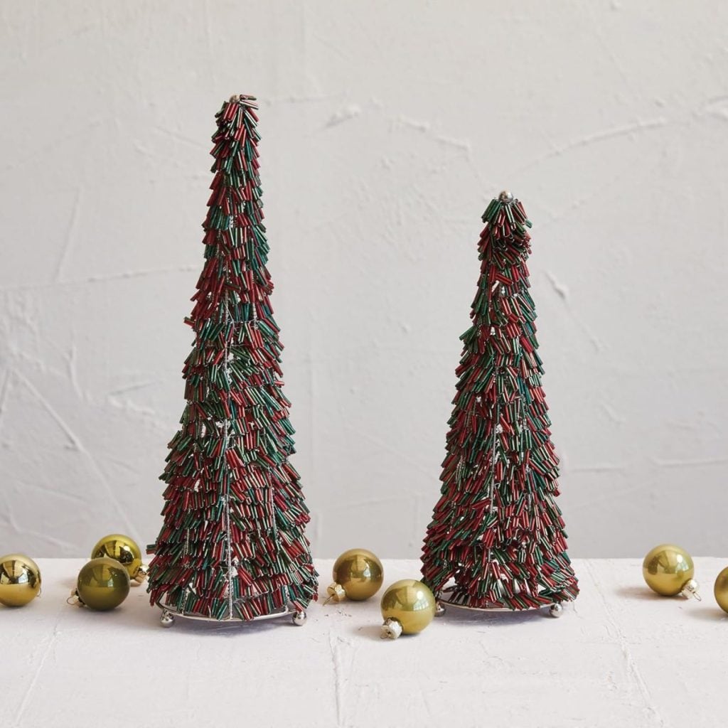 Two cone-shaped Glitter Christmas Trees decorated with red and green sprinkles are displayed on a white surface, surrounded by gold ornaments.