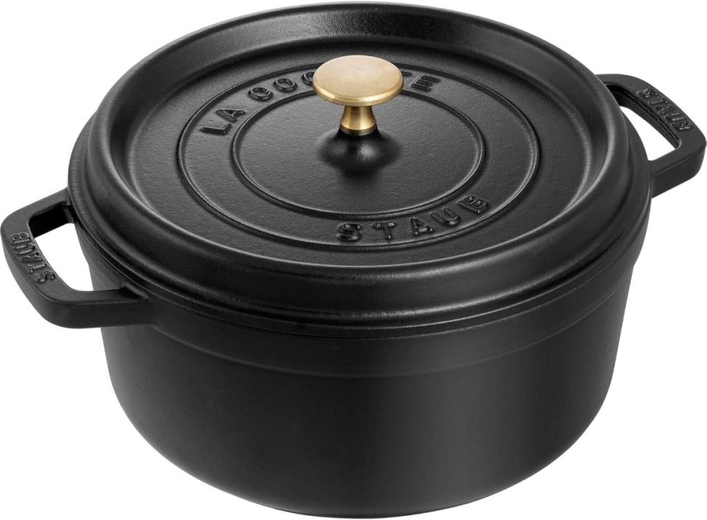 A black cast iron Staub cocotte with a round lid and brass knob, featuring handles on both sides and the words "La Cocotte Staub" embossed on the lid—perfect for baking bread once you’ve learned how to make a sourdough starter.