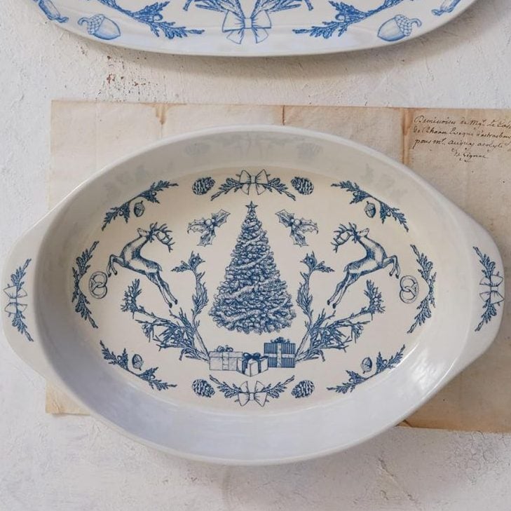 Two ceramic serving dishes with blue holiday-themed designs—one with reindeer, the other with a decorated Christmas tree and presents—are perfect for showcasing your favorite holiday desserts on a light surface.