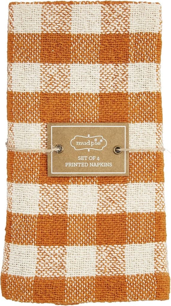 A set of four orange and white checkered cloth napkins, perfect for serving dishes like Marry Me Chicken, folded and tied with a label that reads “Mud Pie Set of 4 Printed Napkins.”.
