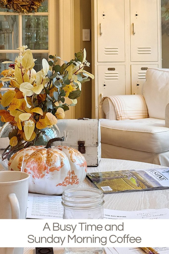A coffee table with fall decor, papers, a mug, a jar, and a painted pumpkin, set in a cozy living room with a sofa and lockers in the background.