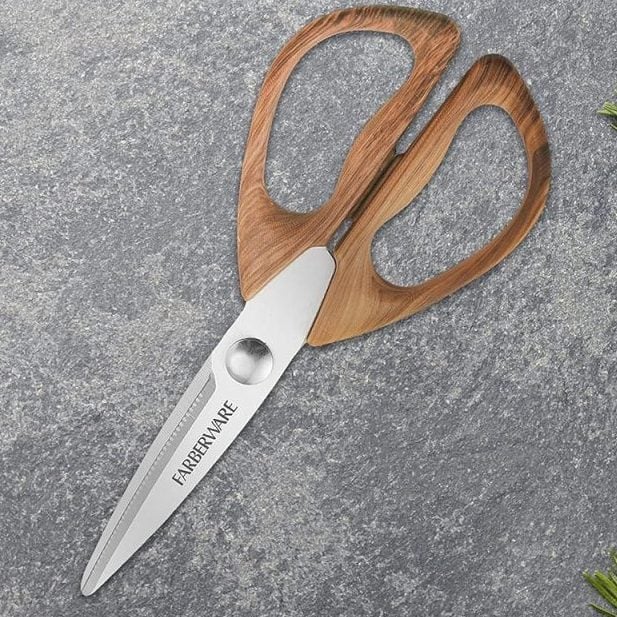 A pair of Farberware kitchen scissors lies on a gray countertop next to bunches of asparagus, tomatoes, carrots, herbs, and a wooden cutting board—ready to help prep a festive Christmas Morning feast.