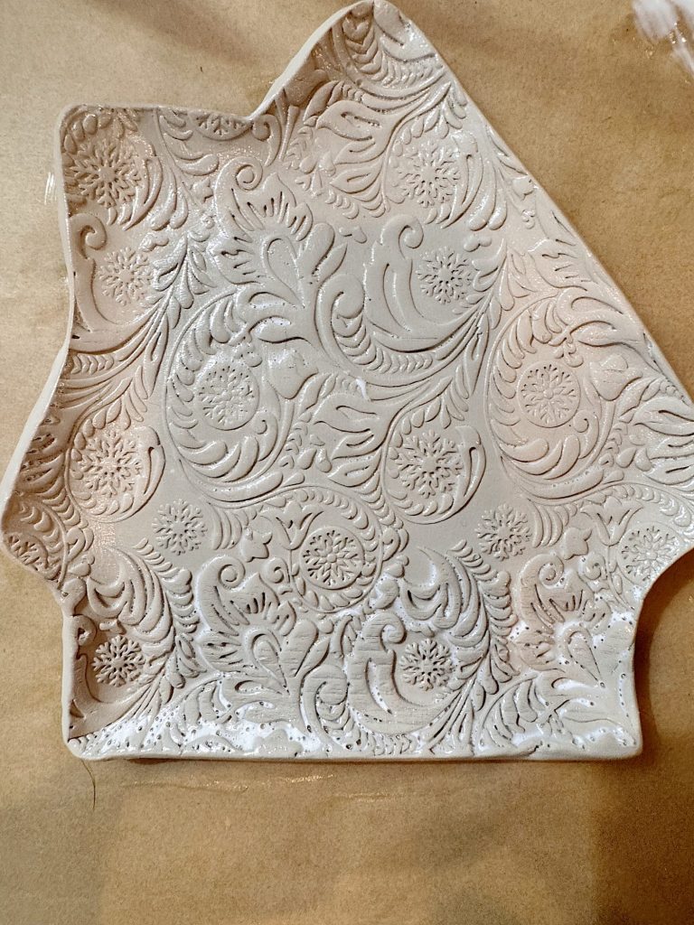 A piece of clay shaped with uneven edges, featuring an intricate floral and paisley embossed pattern on its surface.