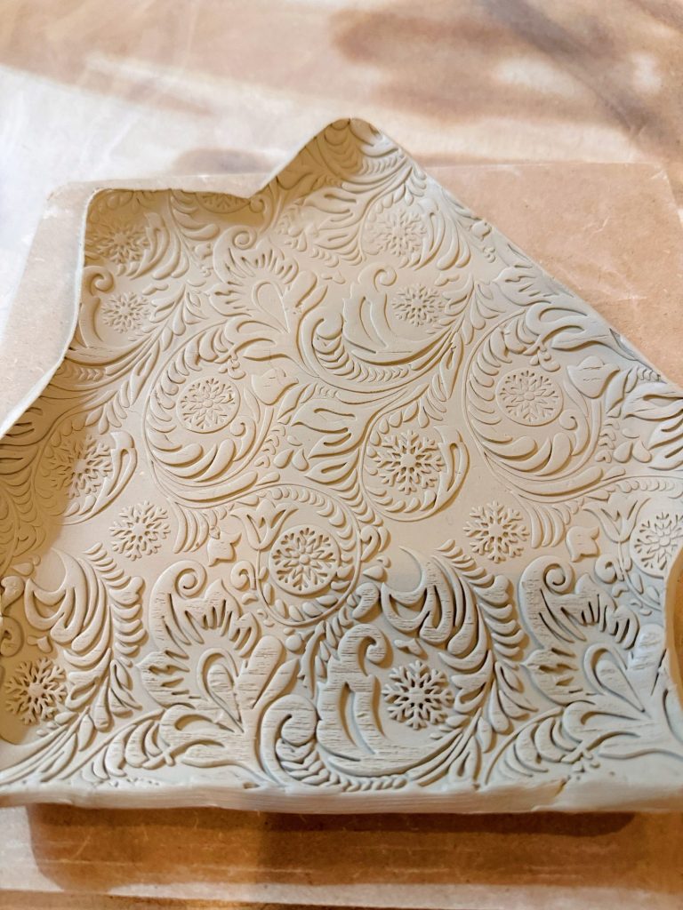 A clay tray shaped like a house with an intricate floral and swirl pattern embossed on its surface.