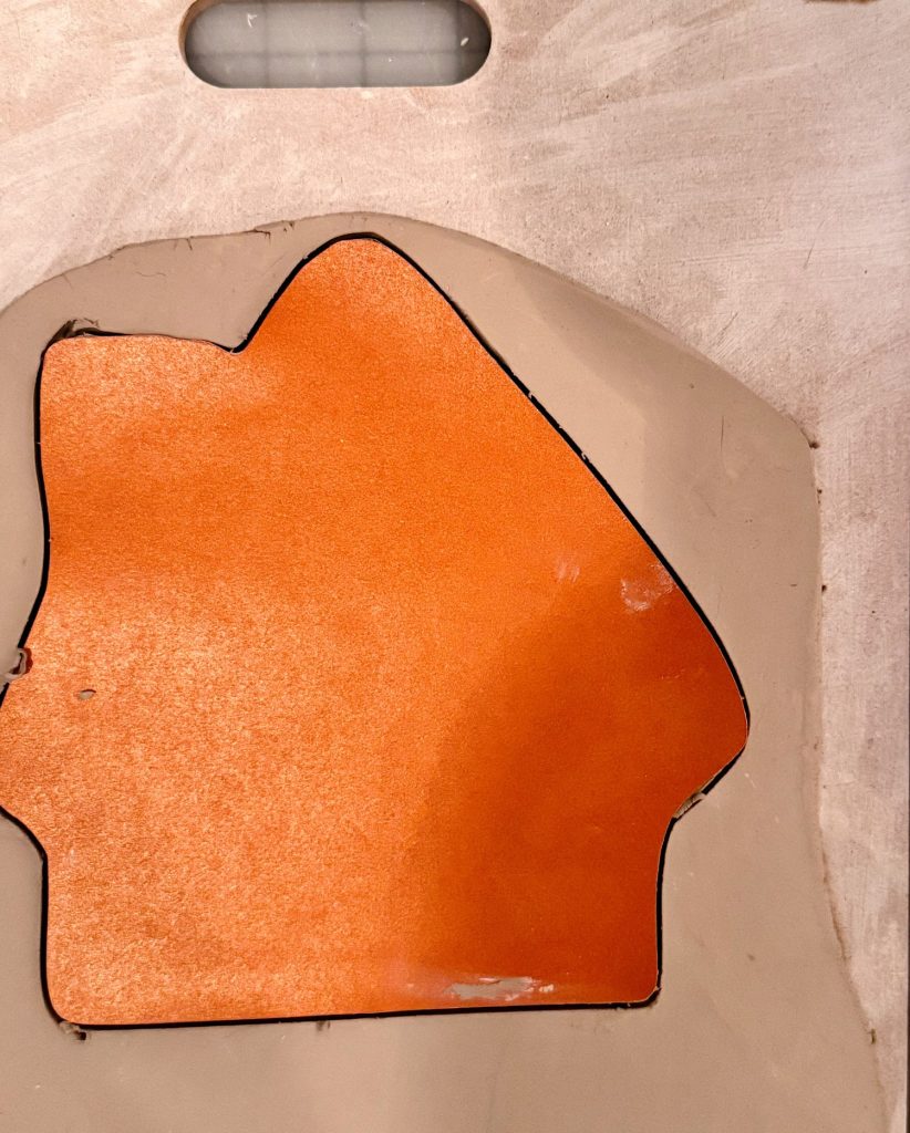 An orange house-shaped piece of material outlined in black rests on a beige surface.