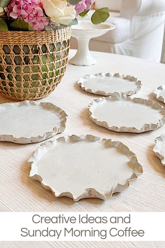 Several irregularly shaped white ceramic plates are arranged on a light wooden table near a woven basket with pink and white flowers. Text reads, "Creative Ideas and Sunday Morning Coffee.