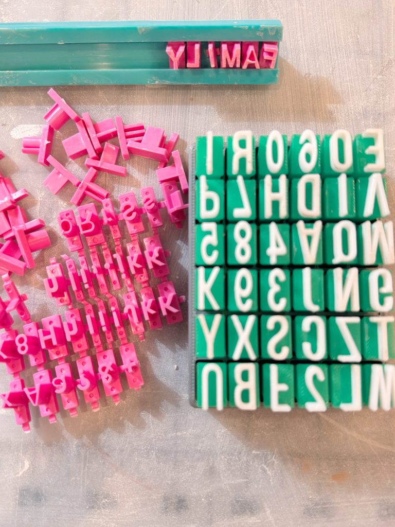 Plastic letter stamps in pink and green are arranged on a flat surface, with some letters assembled in holders and others scattered loosely.