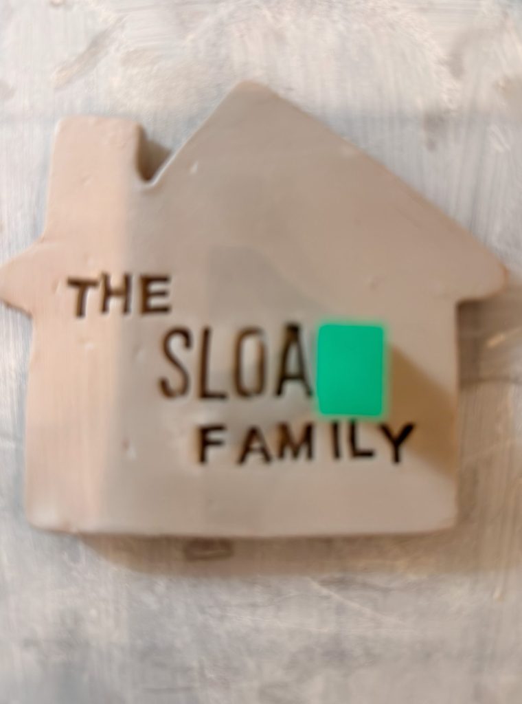 A clay house-shaped plaque reads "THE SLOAN FAMILY," with a small green square covering part of the text.
