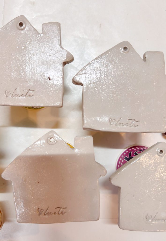 Four small, house-shaped ceramic pieces with the word "blest" engraved on them, arranged on a white surface.