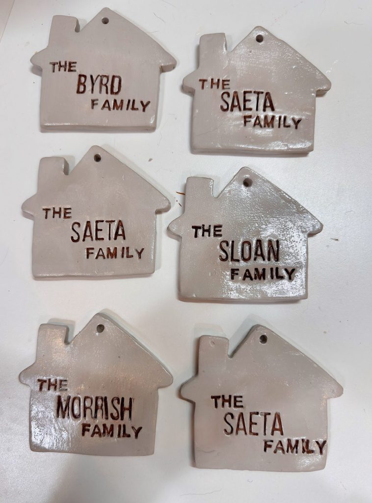 Six clay ornaments shaped like houses, each labeled with a different family name: BYRD, SAETA (three times), SLOAN, and MORASH.