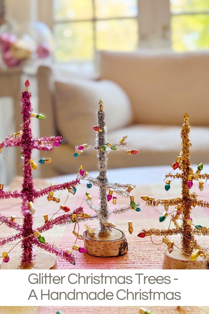 Three small handmade Christmas trees made of glittery pipe cleaners with mini bulb ornaments are displayed on a table indoors.