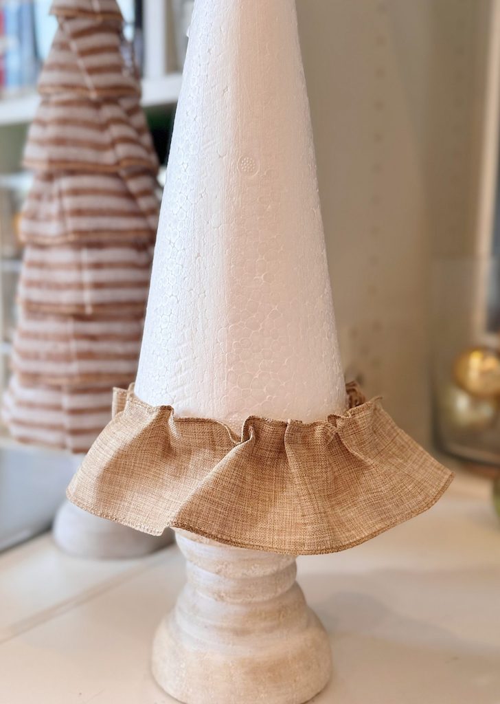 A white cone-shaped object with a textured surface stands on a wooden base and is wrapped with a ruffled beige fabric near the bottom.