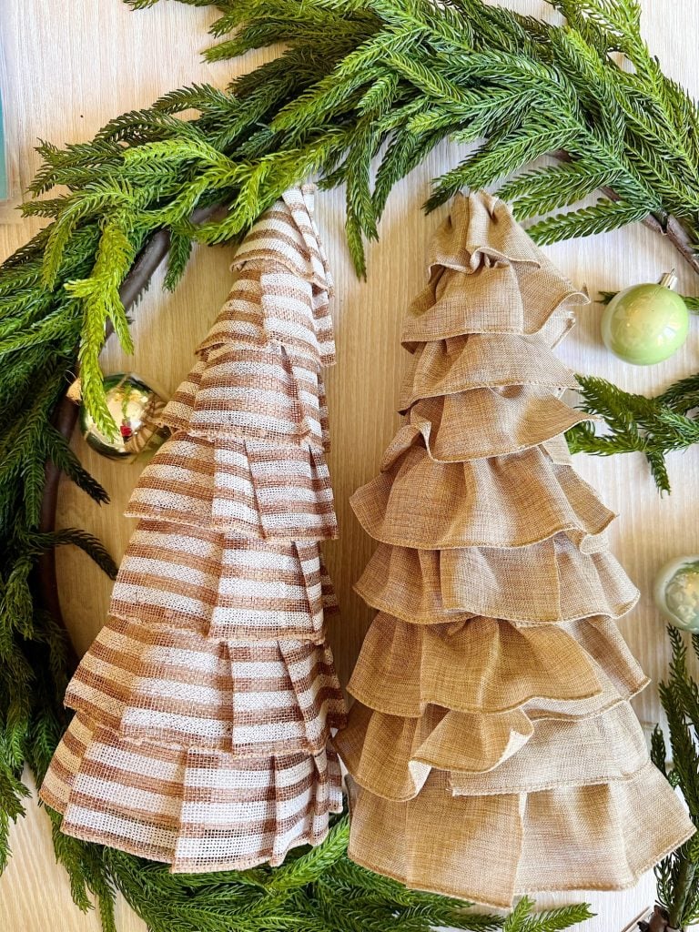 Two fabric Christmas trees with layered ruffles, one striped and one solid, are displayed within a green wreath with ornaments.