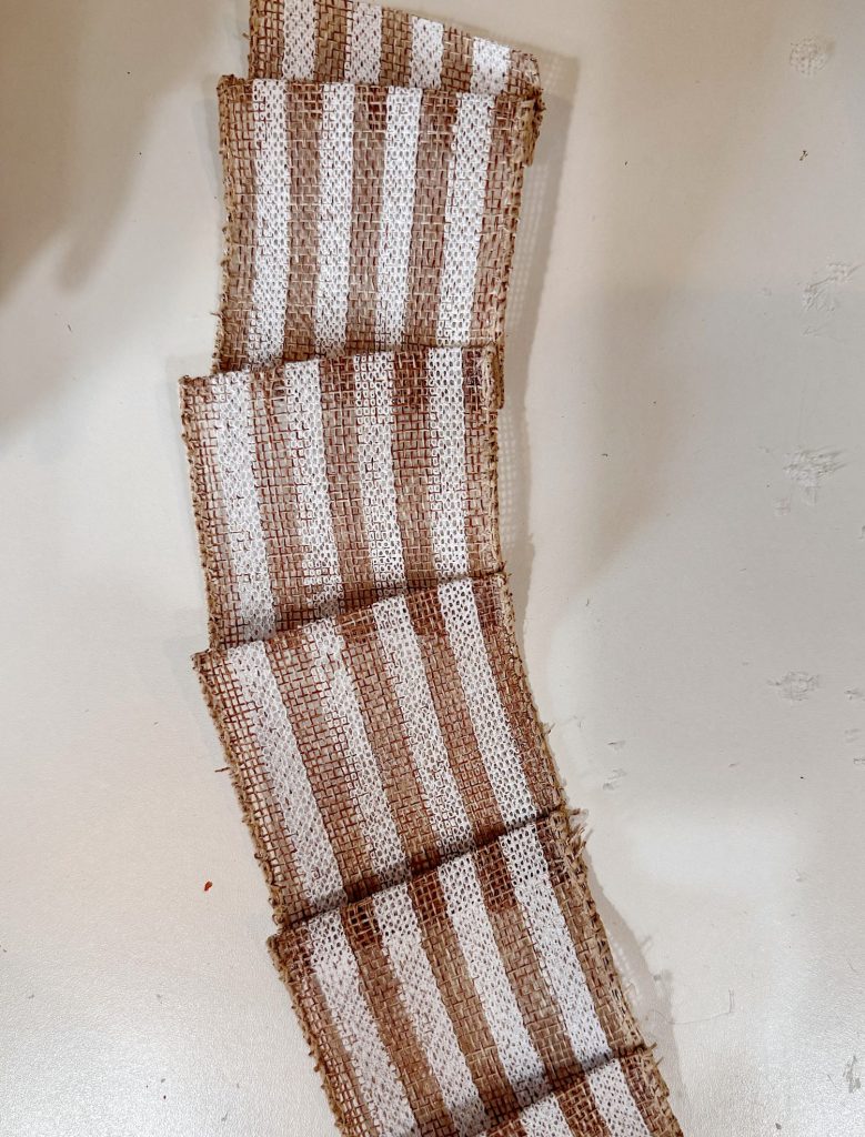 A piece of burlap ribbon with alternating brown and white vertical stripes is laid out in a zigzag pattern on a light-colored surface.