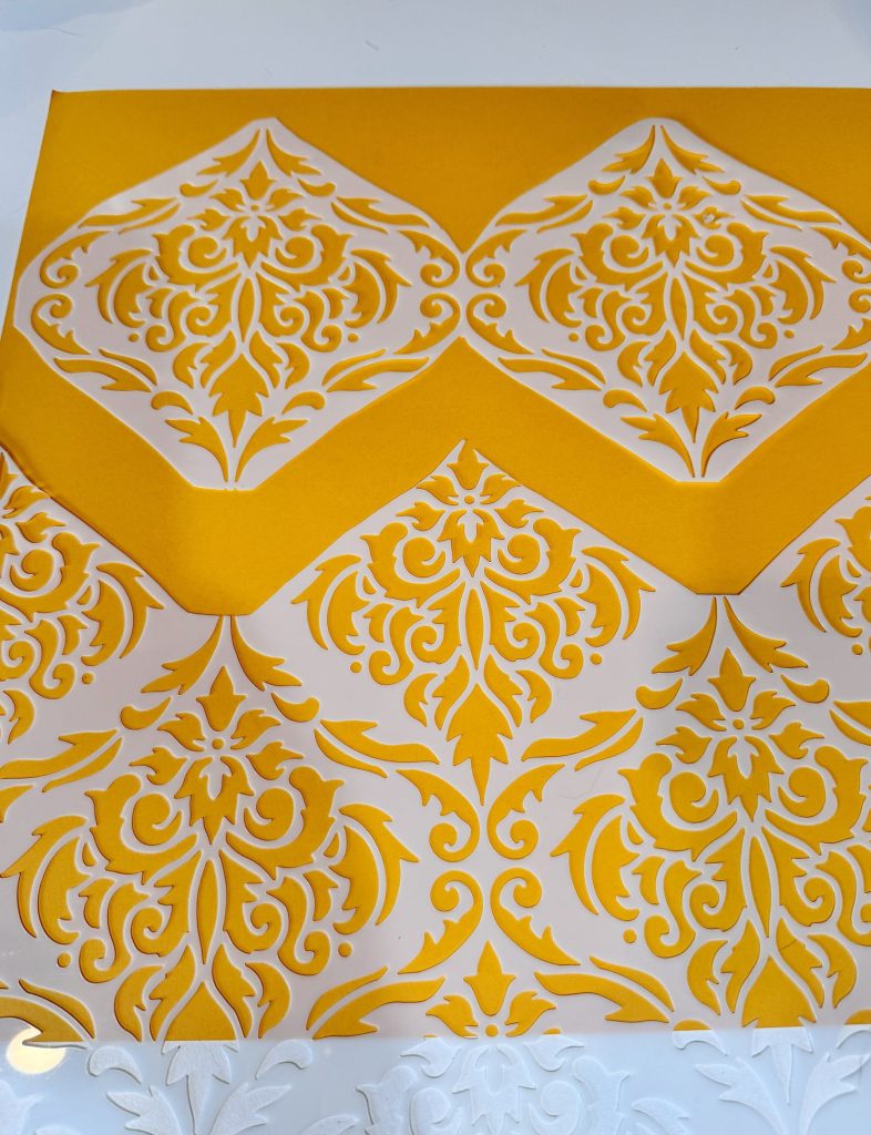 A sheet of yellow and white paper featuring an ornate, symmetrical cutout pattern with floral and geometric motifs.