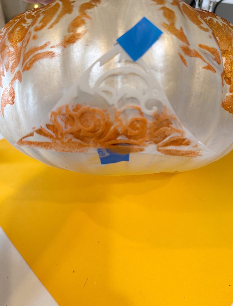 Close-up of a translucent bowl with orange decorative patterns and blue tape applied, resting on a bright yellow surface.