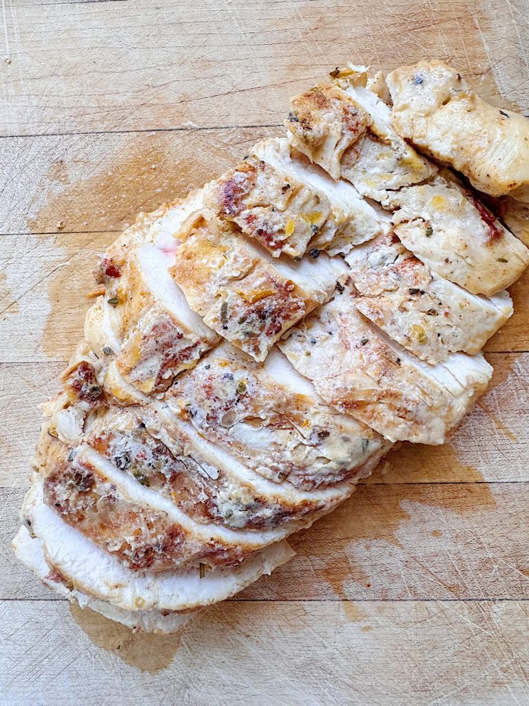 Sliced cooked chicken breast with seasoning on a wooden cutting board.