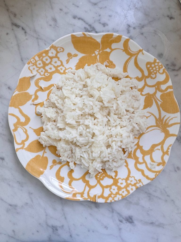 A serving of plain white rice on a yellow and white floral-patterned plate, placed on a marble surface.