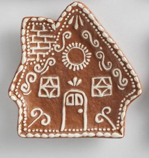 A brown ceramic plate shaped like a house, decorated with white icing-like patterns resembling a gingerbread house.