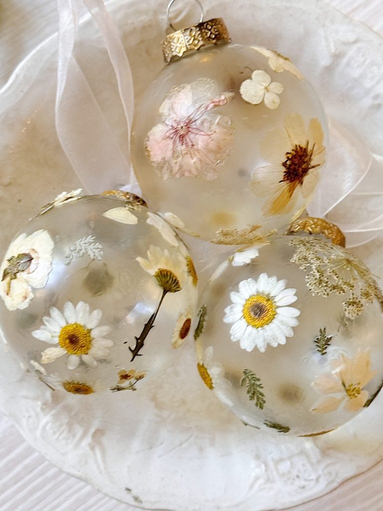 Three clear glass ornaments filled with dried flowers rest on a white ceramic plate.